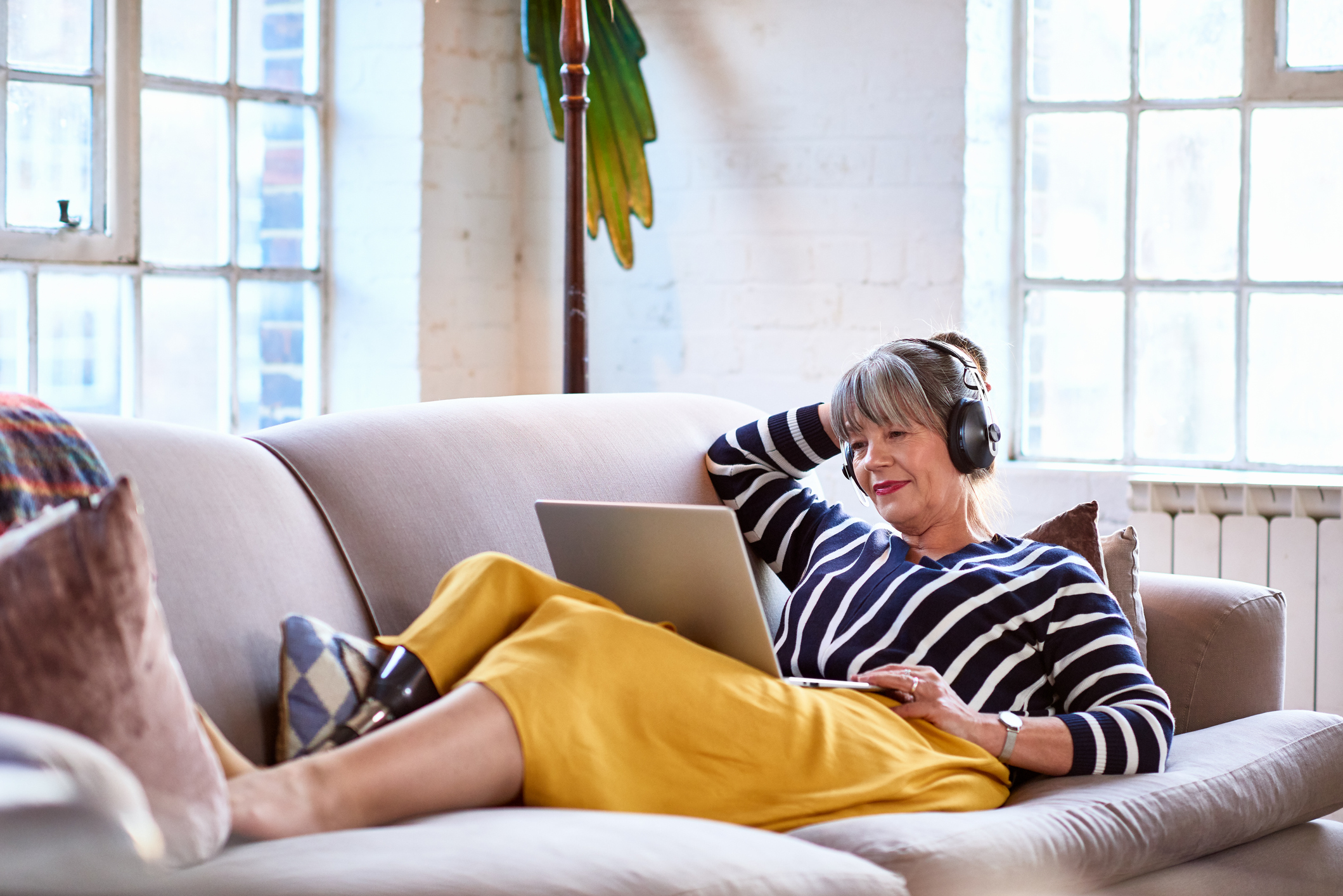 Senior woman wearing headphones watching movie on laptop relaxed woman