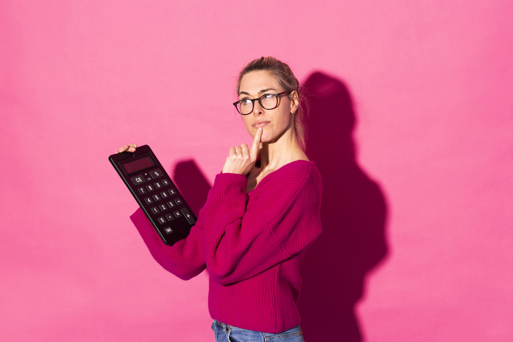 Thoughtful woman gesturing and holding calculator against pink background Russell Brand