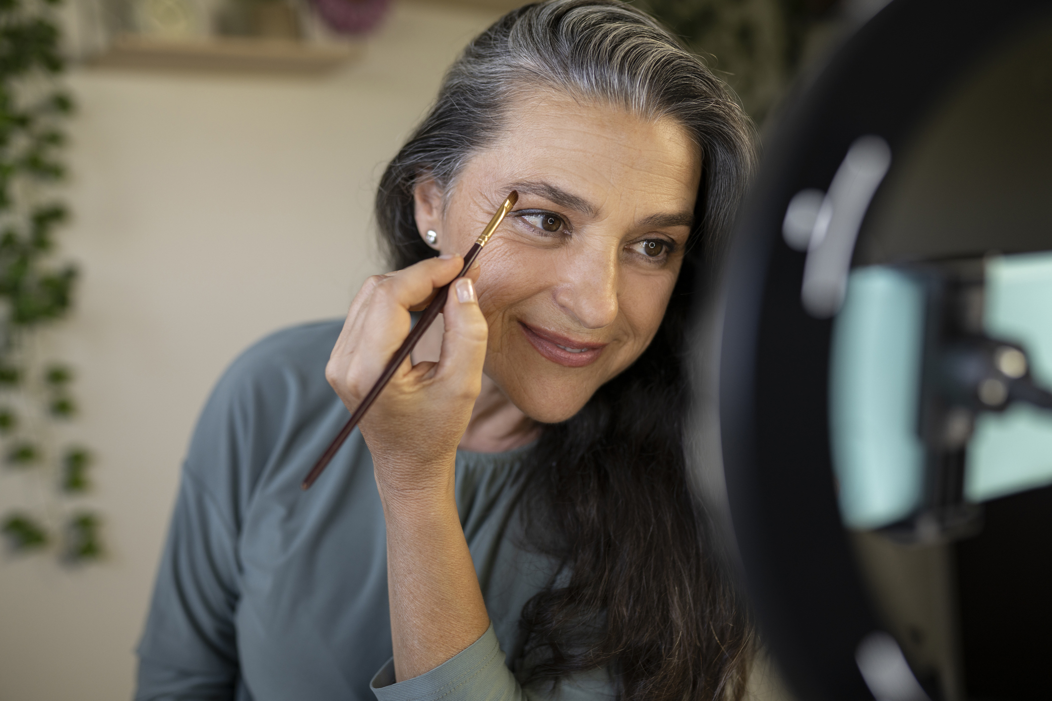 Smiling female vlogger brushing eyebrows during tutorial at home Jennifer Aniston