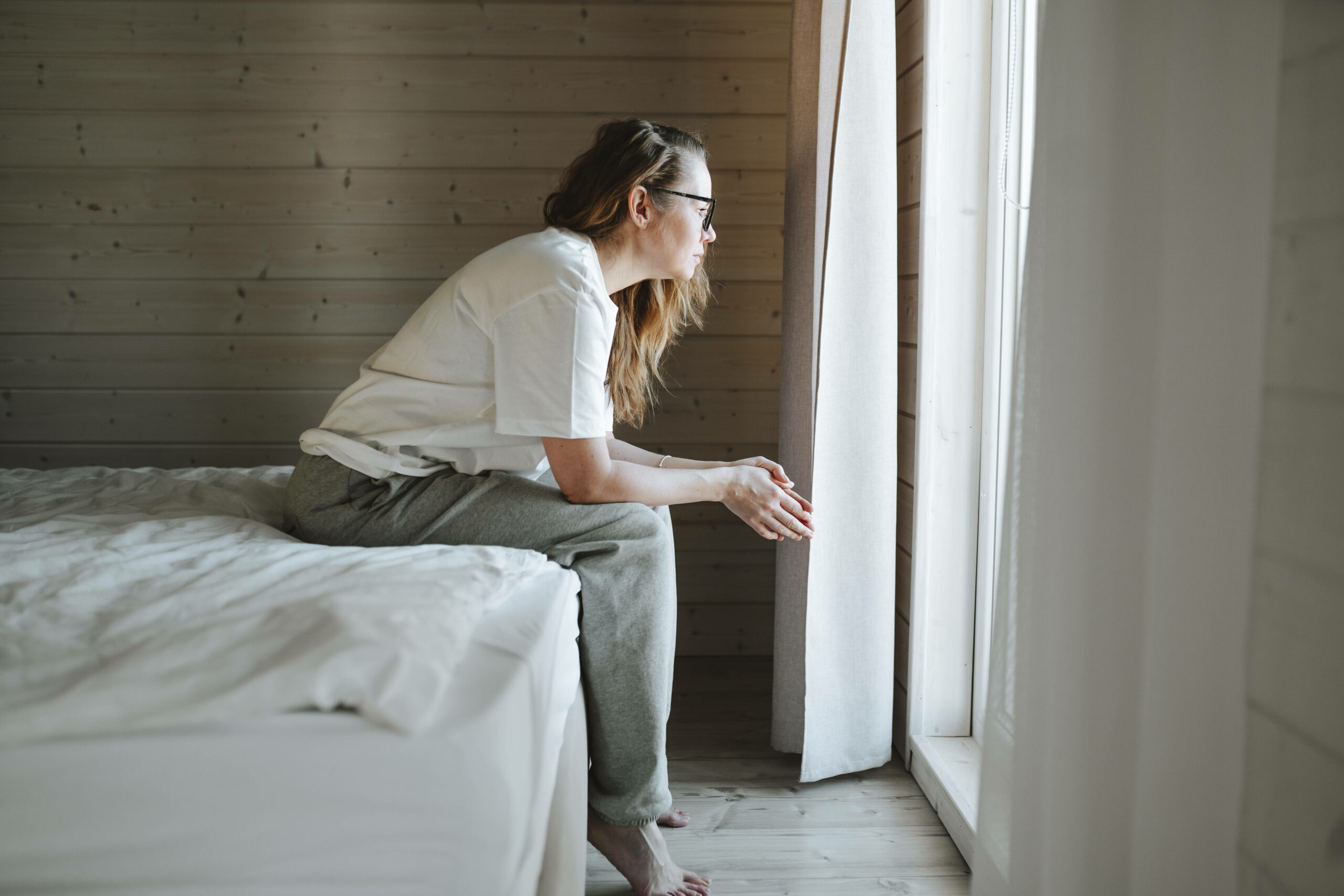 Worried woman sitting on bed and looking through window at home model released, Symbolfoto property released, OLRF00200 Jennifer Aniston