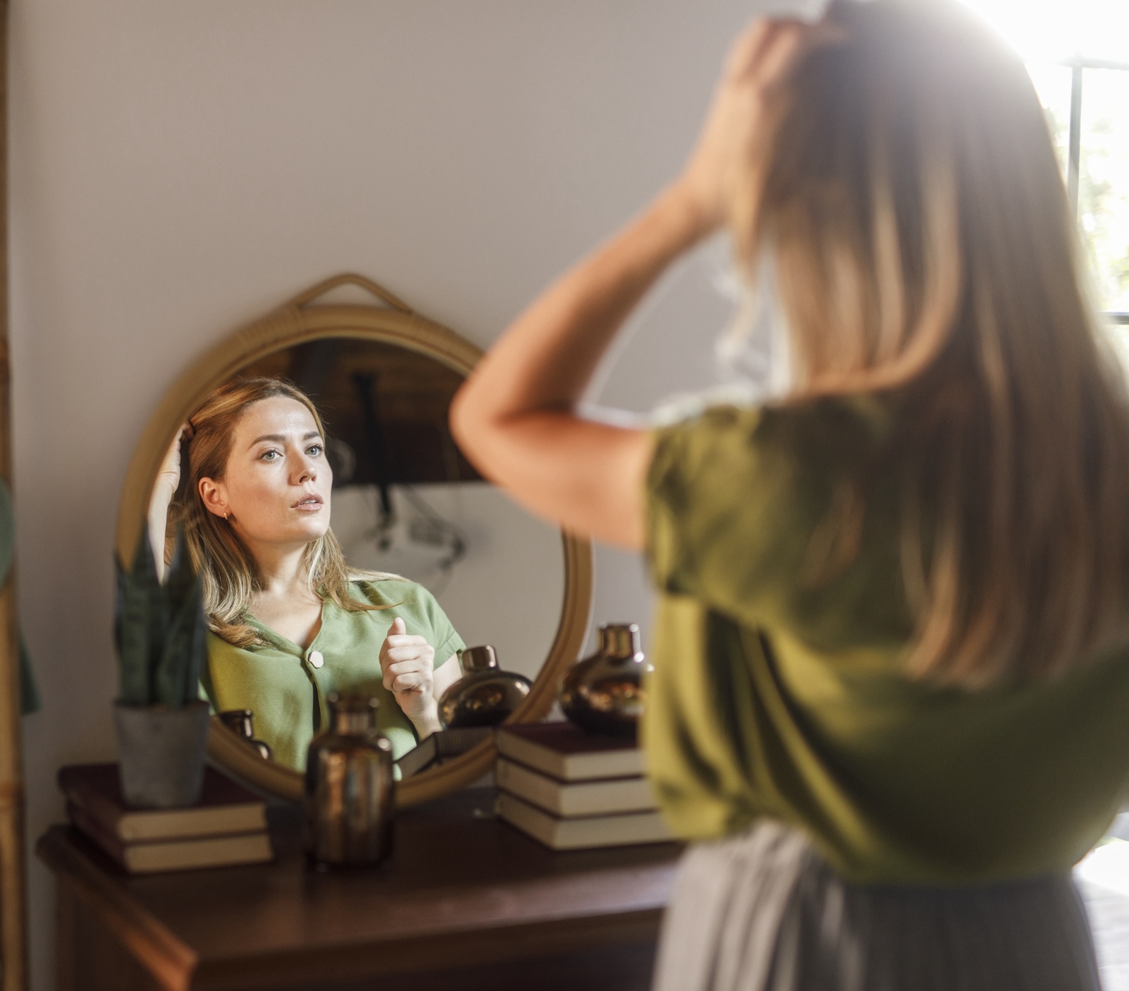 Woman looking in the mirror and examining her skin and hair Woman looking in mirror