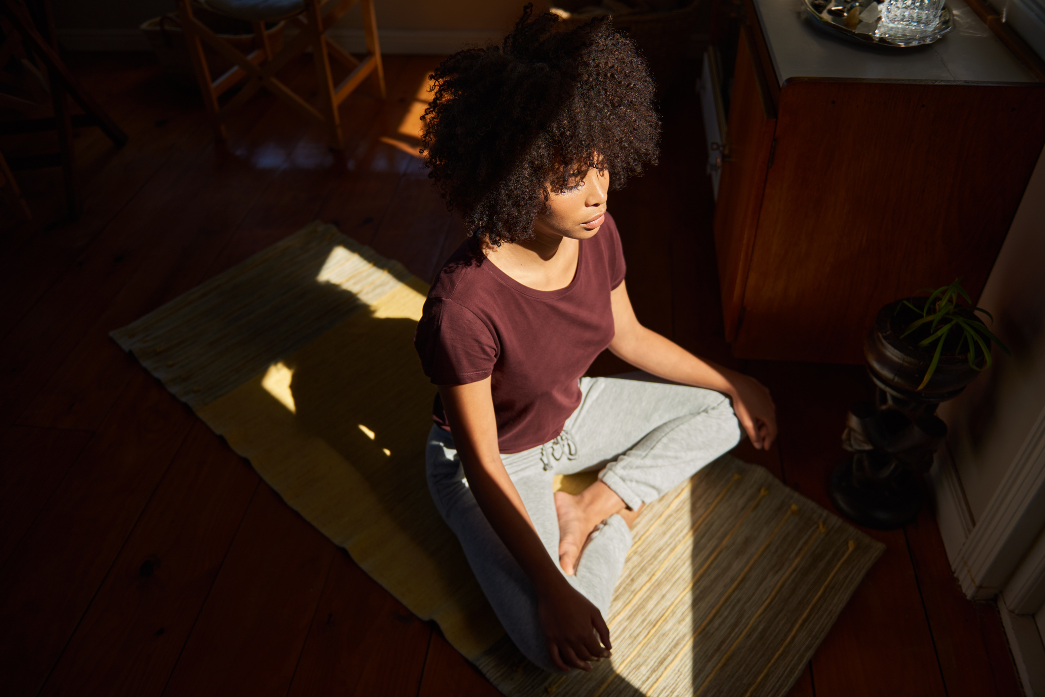 Young African woman meditating by a sunny window at home Woman meditating