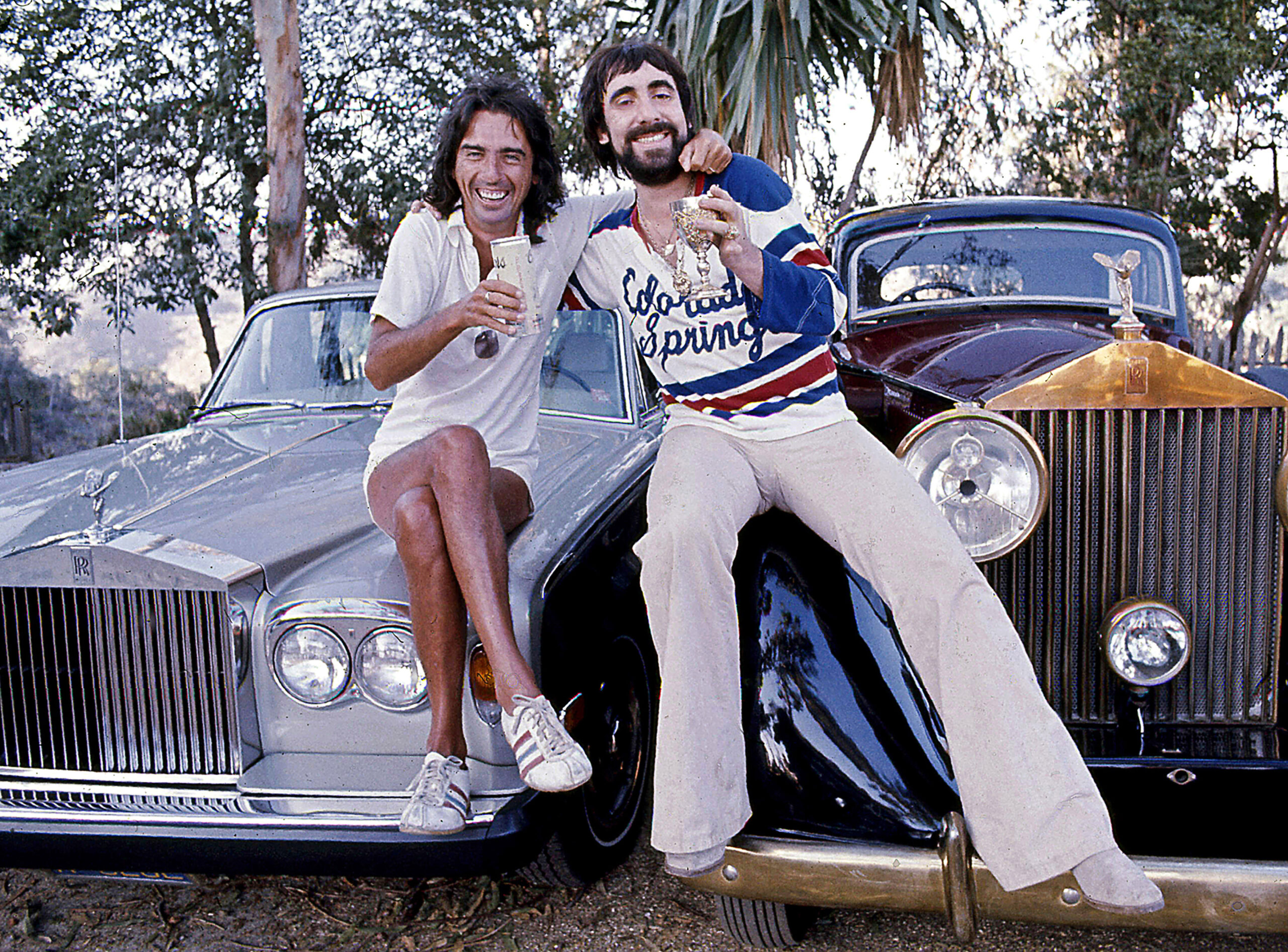 Singer Alice Cooper And His Friend, Keith Moon, The Who's Celebrated Drummer Sitting On the Hoods Of Their Rolls-Royce Cars On Mulholland Drive In The Hollywood Hills In Los Angeles, California, June 1976.