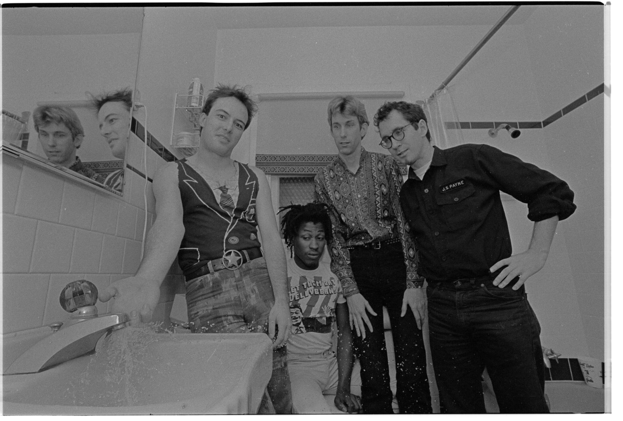 The members of the punk rock group The Dead Kennedys (from left: Jello Biafra, D. H. Peligro, East Bay Ray, Klaus Flouride) stand in the doorway of a bathroom as Jello sticks his finger under the running water of the bathroom sink.
